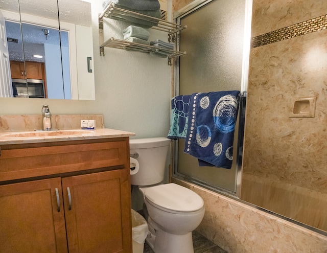 full bathroom with enclosed tub / shower combo, vanity, toilet, and a textured ceiling