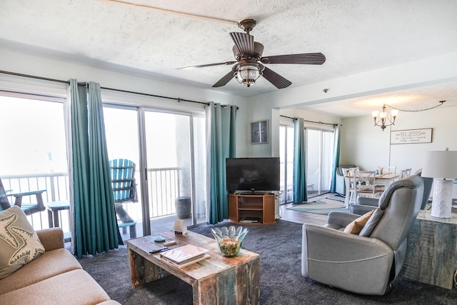 living room featuring ceiling fan with notable chandelier, a wealth of natural light, a textured ceiling, and dark carpet