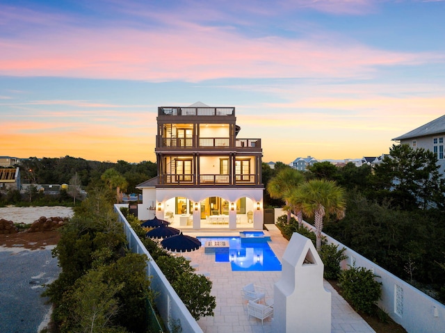 back house at dusk with a fenced in pool, a patio, and a balcony