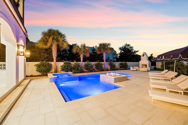 pool at dusk featuring a patio area and an in ground hot tub