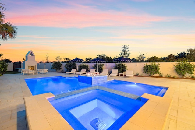 pool at dusk with an in ground hot tub and a patio area