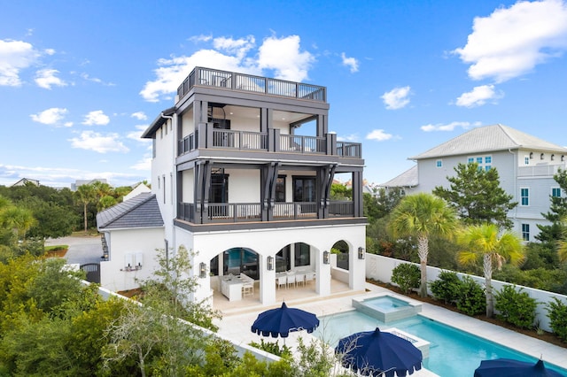 rear view of house featuring a swimming pool with hot tub, a patio, and a balcony