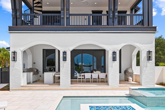 rear view of house featuring a pool with hot tub, a patio, an outdoor kitchen, and a balcony