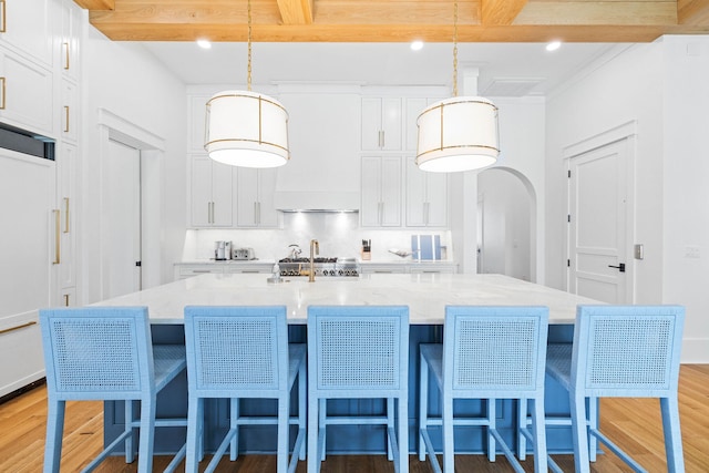 kitchen featuring wood-type flooring, white cabinetry, a large island, hanging light fixtures, and beamed ceiling