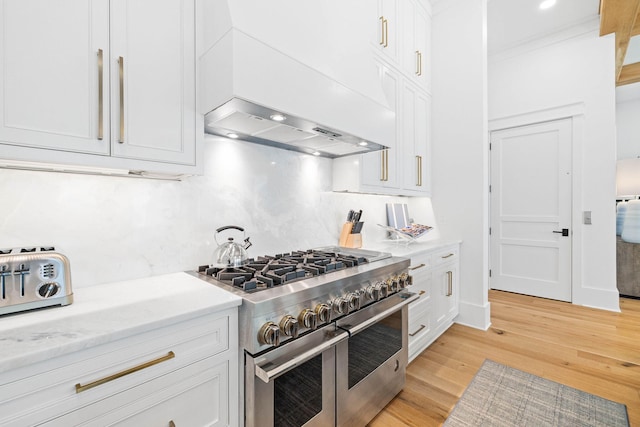 kitchen featuring range with two ovens, light hardwood / wood-style floors, white cabinets, and wall chimney range hood