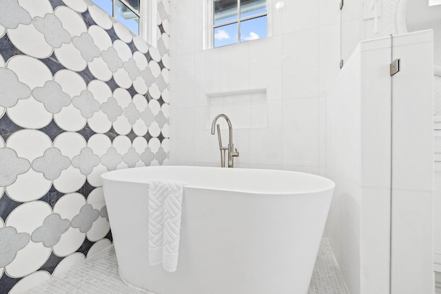 bathroom with a tub to relax in, tile walls, and tile patterned floors