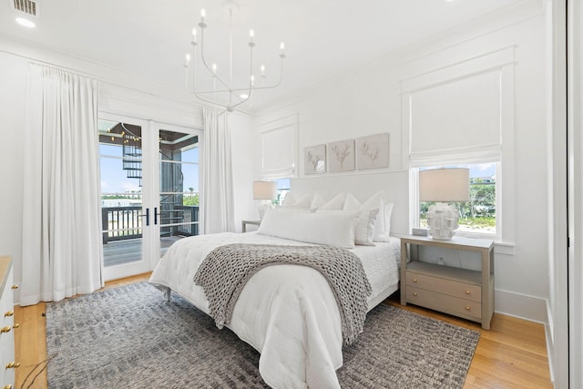 bedroom with access to exterior, light wood-type flooring, french doors, and a notable chandelier