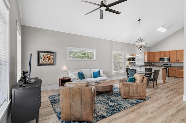 living room with light hardwood / wood-style floors, ceiling fan with notable chandelier, and high vaulted ceiling