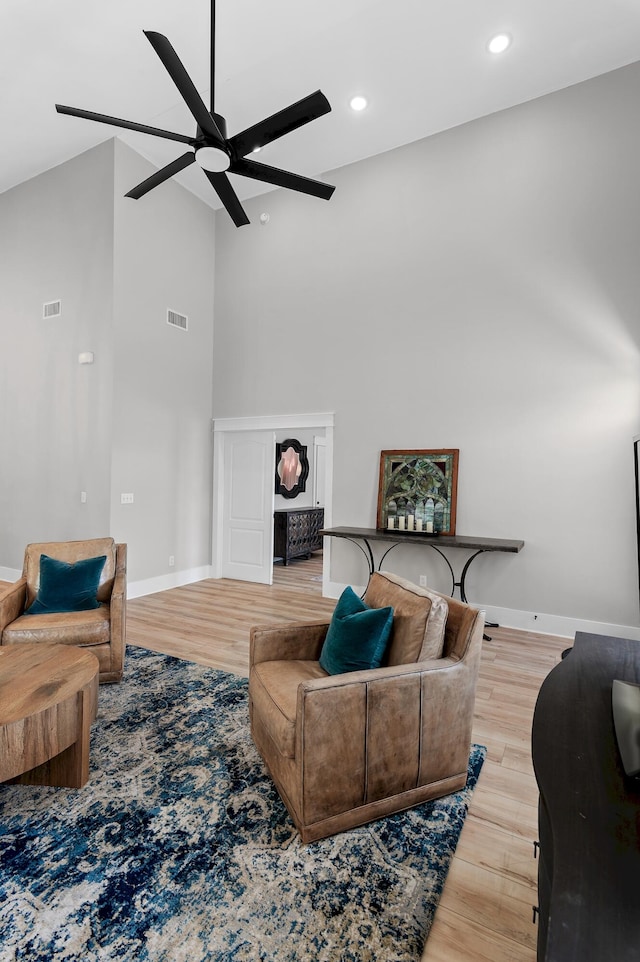 living room featuring ceiling fan, light hardwood / wood-style floors, and a towering ceiling