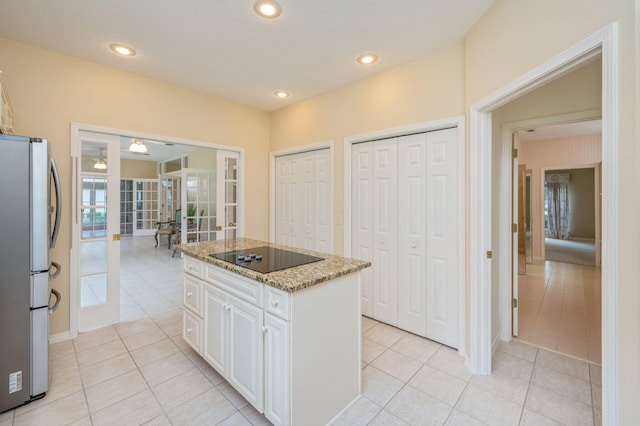 kitchen with white cabinetry, light tile patterned flooring, stainless steel fridge, black electric stovetop, and a kitchen island