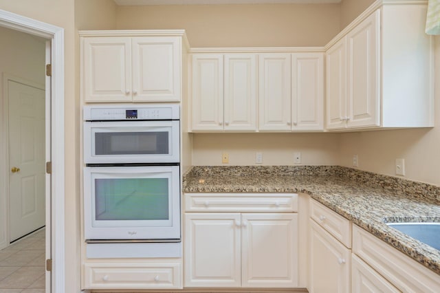 kitchen with light tile patterned floors, white cabinetry, light stone counters, and double oven