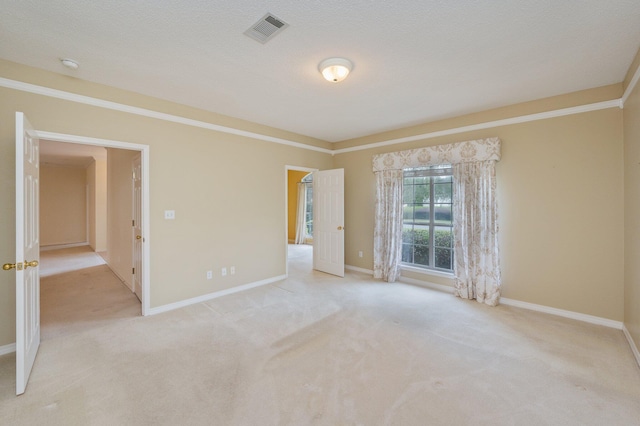 spare room with light colored carpet, ornamental molding, and a textured ceiling