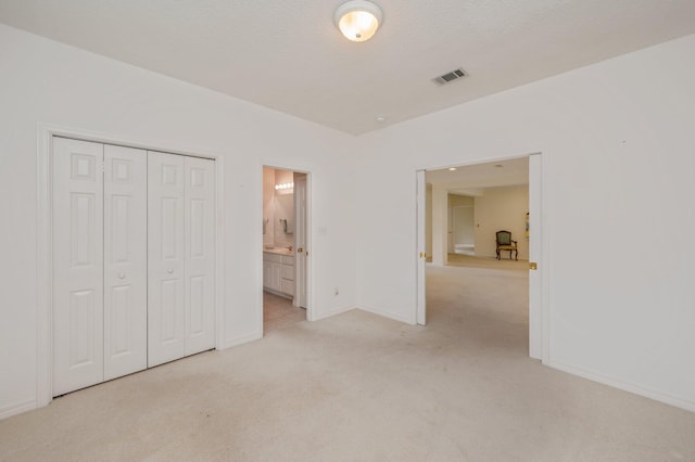 unfurnished bedroom with a textured ceiling, ensuite bathroom, light carpet, and a closet