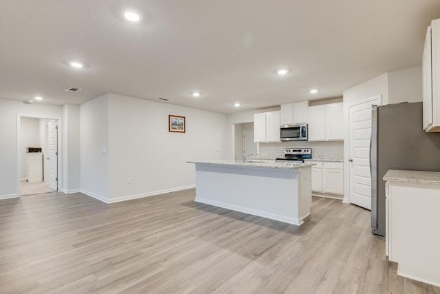 kitchen with appliances with stainless steel finishes, light stone countertops, an island with sink, white cabinets, and light wood-type flooring