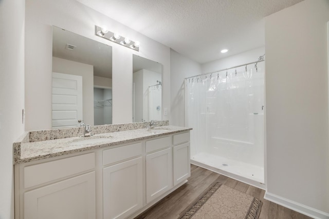 bathroom with walk in shower, vanity, wood-type flooring, and a textured ceiling