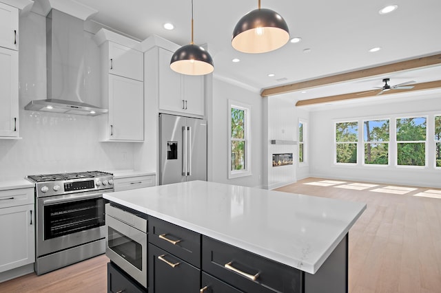 kitchen with pendant lighting, a healthy amount of sunlight, high quality appliances, and wall chimney range hood