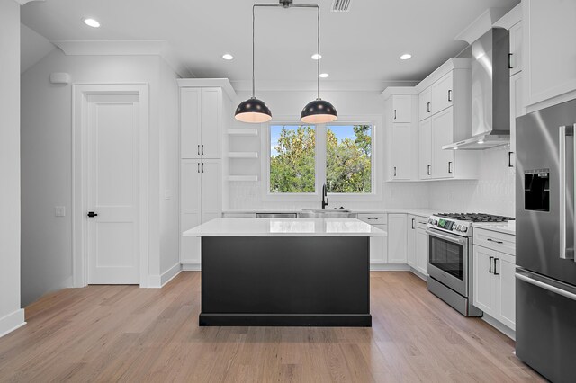 kitchen with a center island, wall chimney exhaust hood, hanging light fixtures, white cabinetry, and appliances with stainless steel finishes