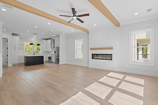 unfurnished living room featuring a healthy amount of sunlight, light wood-type flooring, a fireplace, and beamed ceiling