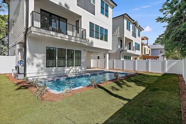 back of house featuring a balcony, a lawn, and a fenced in pool