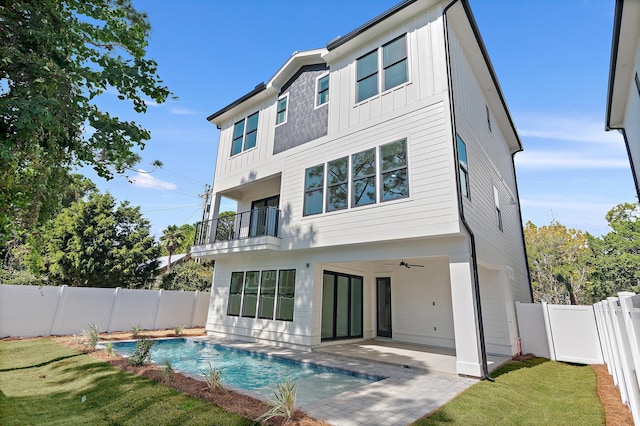 back of house with a balcony, ceiling fan, a fenced in pool, a patio, and a lawn