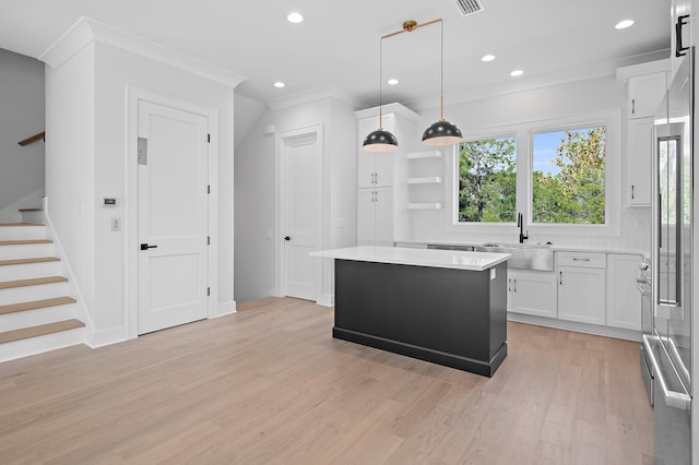 kitchen featuring a center island, hanging light fixtures, sink, white cabinetry, and light wood-type flooring