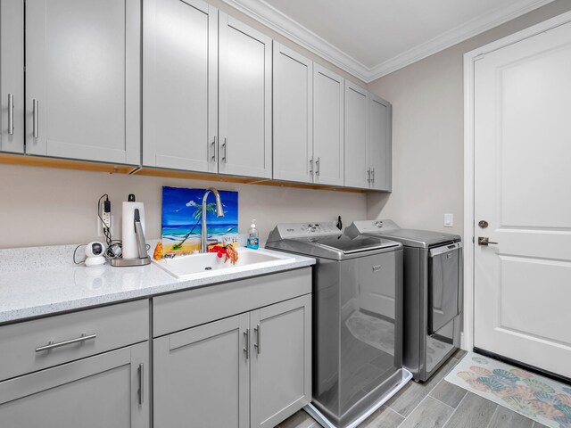 clothes washing area featuring cabinets, sink, light hardwood / wood-style flooring, crown molding, and washer and dryer