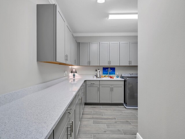 kitchen featuring light stone counters, ornamental molding, washer / dryer, light hardwood / wood-style flooring, and gray cabinetry