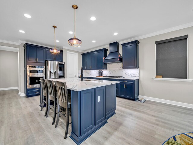 kitchen with stainless steel appliances, sink, a kitchen island with sink, custom range hood, and decorative light fixtures