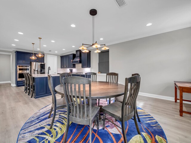 dining room with sink, light wood-type flooring, and crown molding