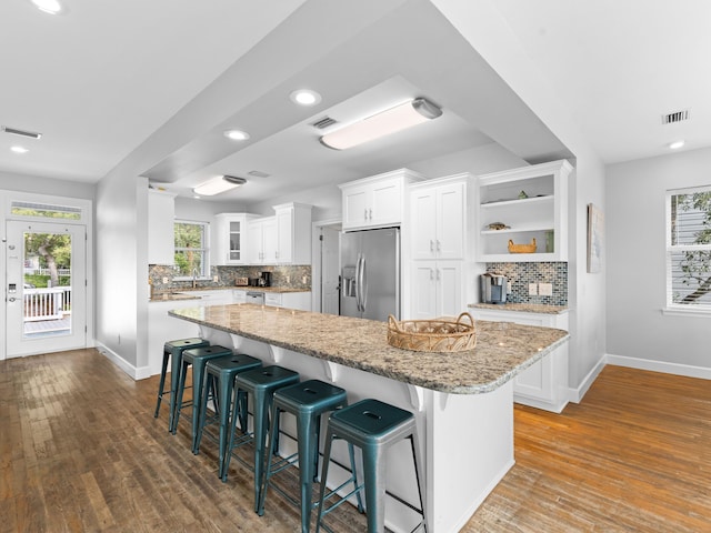 kitchen featuring a healthy amount of sunlight, white cabinets, stainless steel refrigerator with ice dispenser, hardwood / wood-style floors, and backsplash