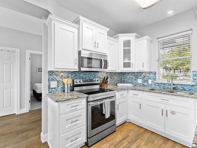 kitchen with light hardwood / wood-style floors, white cabinets, sink, tasteful backsplash, and appliances with stainless steel finishes