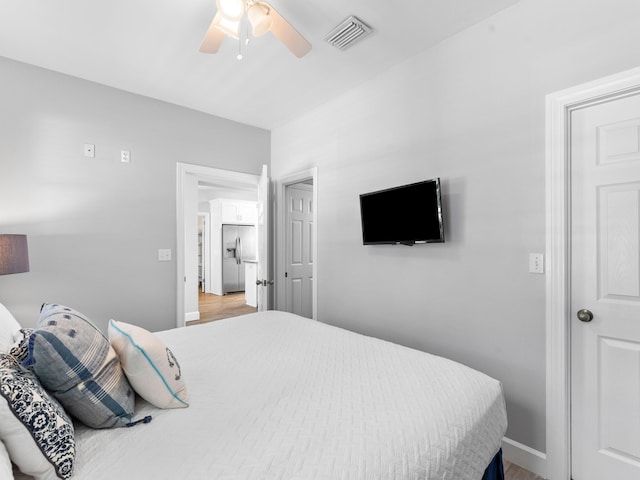 bedroom with stainless steel refrigerator with ice dispenser, ceiling fan, and wood-type flooring