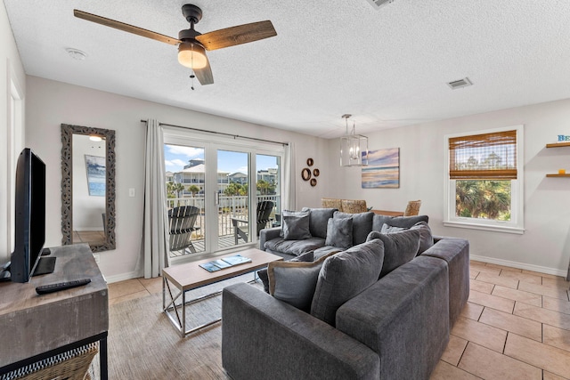 tiled living room with ceiling fan with notable chandelier and a textured ceiling