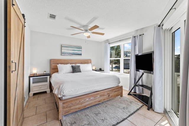 bedroom featuring a barn door, light tile patterned floors, ceiling fan, and a textured ceiling