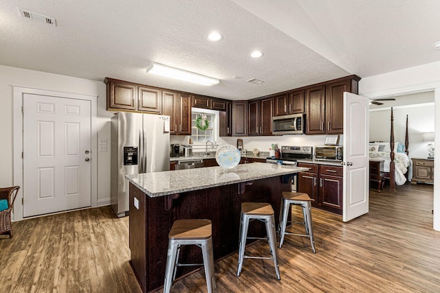 kitchen with a kitchen island, appliances with stainless steel finishes, a textured ceiling, a breakfast bar, and dark wood-type flooring