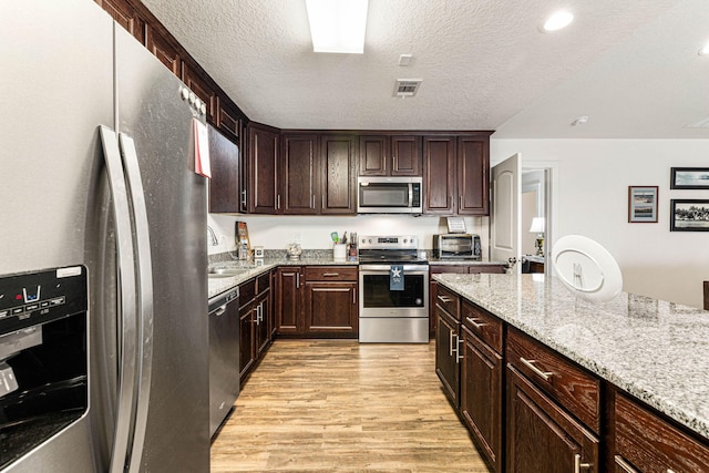 kitchen with stainless steel appliances, light hardwood / wood-style floors, light stone countertops, and a textured ceiling