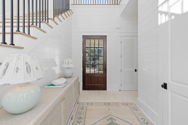 entryway featuring wood walls, a towering ceiling, and light tile patterned flooring