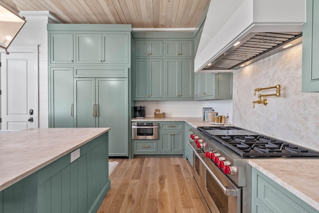 kitchen featuring premium range hood, green cabinets, decorative backsplash, premium appliances, and light hardwood / wood-style floors