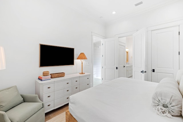 bedroom featuring connected bathroom, light hardwood / wood-style floors, and ornamental molding