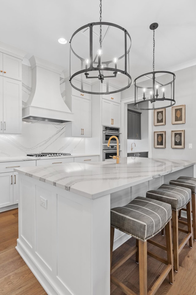 kitchen featuring white cabinetry, a large island, custom exhaust hood, double oven, and light hardwood / wood-style flooring