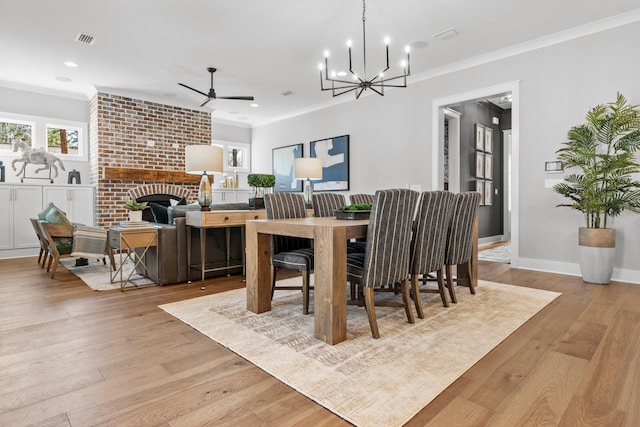 dining room with a brick fireplace, ceiling fan with notable chandelier, light hardwood / wood-style flooring, and ornamental molding