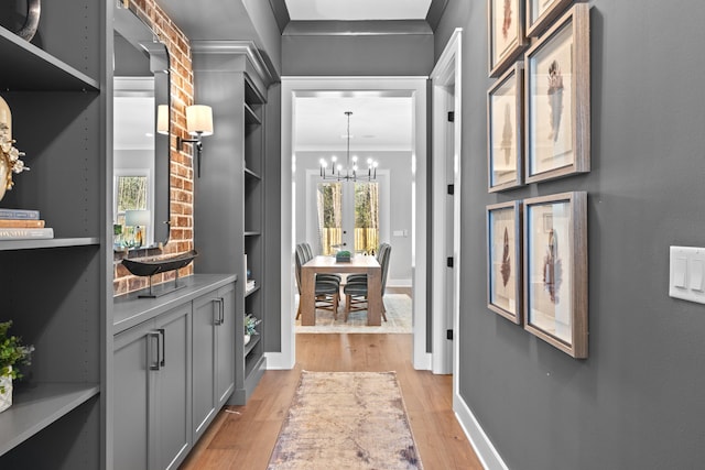 corridor featuring a notable chandelier, light hardwood / wood-style floors, and crown molding