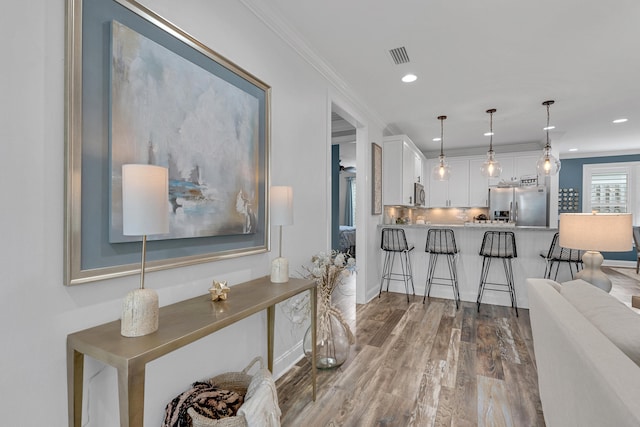 interior space featuring wood-type flooring, stainless steel appliances, white cabinets, pendant lighting, and a breakfast bar area