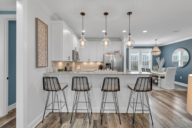 kitchen featuring light stone counters, stainless steel appliances, a kitchen bar, hardwood / wood-style floors, and white cabinets