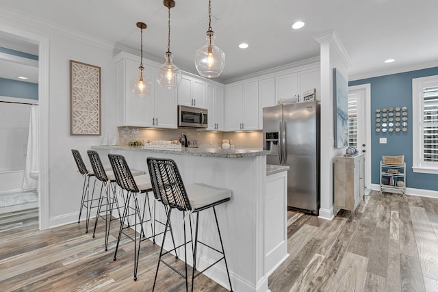 kitchen with white cabinets, kitchen peninsula, light hardwood / wood-style flooring, pendant lighting, and appliances with stainless steel finishes