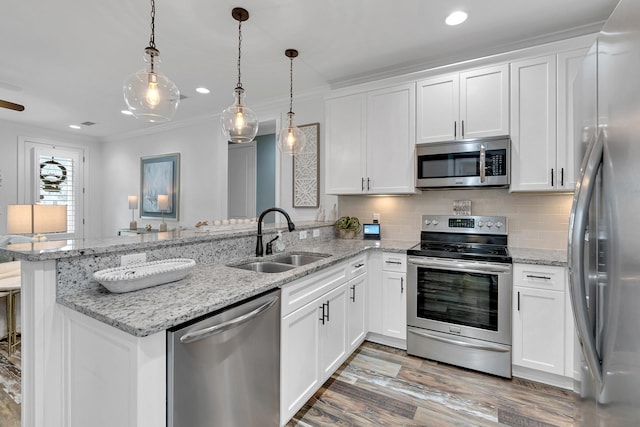 kitchen featuring stainless steel appliances, white cabinetry, sink, kitchen peninsula, and decorative light fixtures