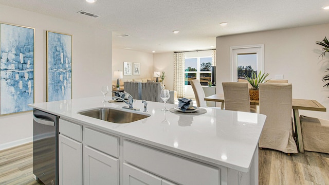 kitchen with light hardwood / wood-style floors, sink, a textured ceiling, a kitchen island with sink, and white cabinets