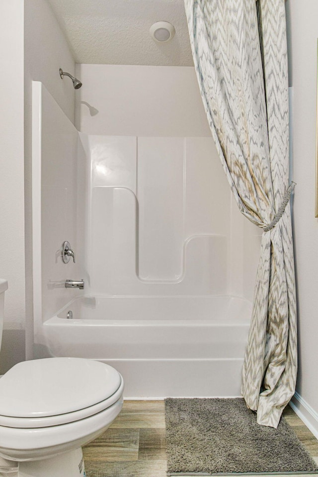 bathroom featuring a textured ceiling, hardwood / wood-style flooring, toilet, and shower / bathtub combination with curtain