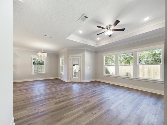 unfurnished living room with wood-type flooring, ceiling fan with notable chandelier, a tray ceiling, and ornamental molding