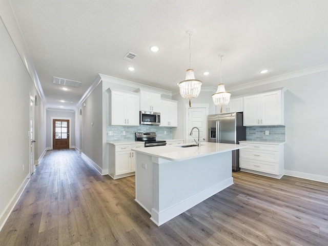 kitchen featuring pendant lighting, white cabinets, appliances with stainless steel finishes, backsplash, and a kitchen island with sink